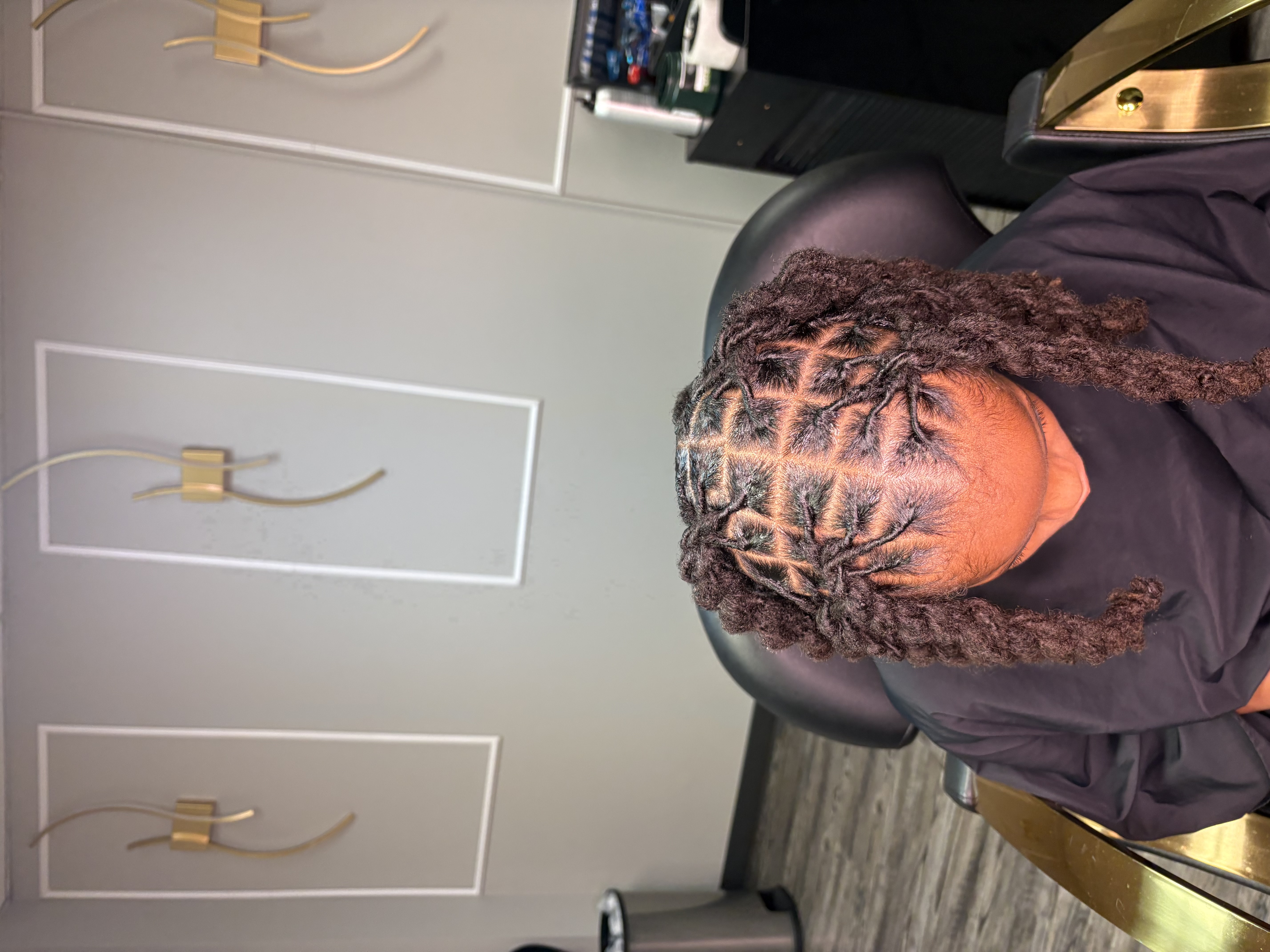 Client in black cape, complex geometric cornrow pattern